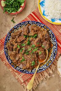 photo of kebab halla on a colorful plate with rice on another plate in the background.