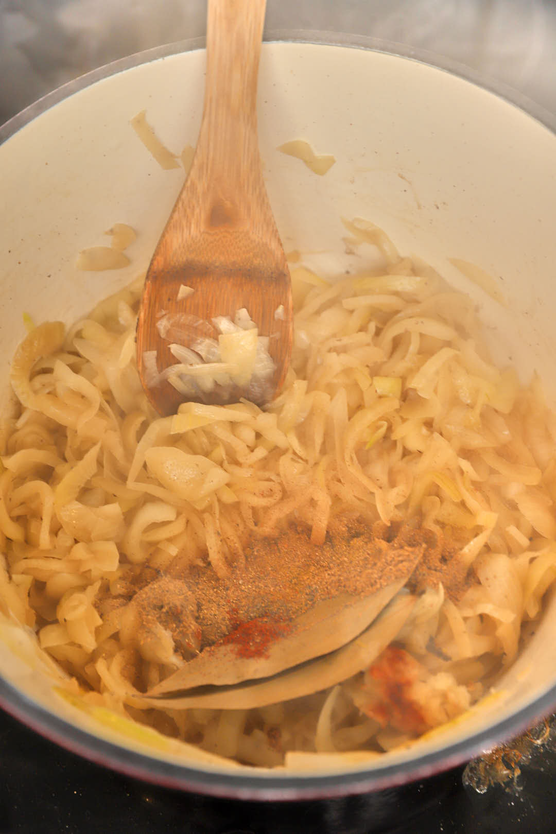 spices, bay leaves and tomato paste added to softened sliced yellow onions in a pot.