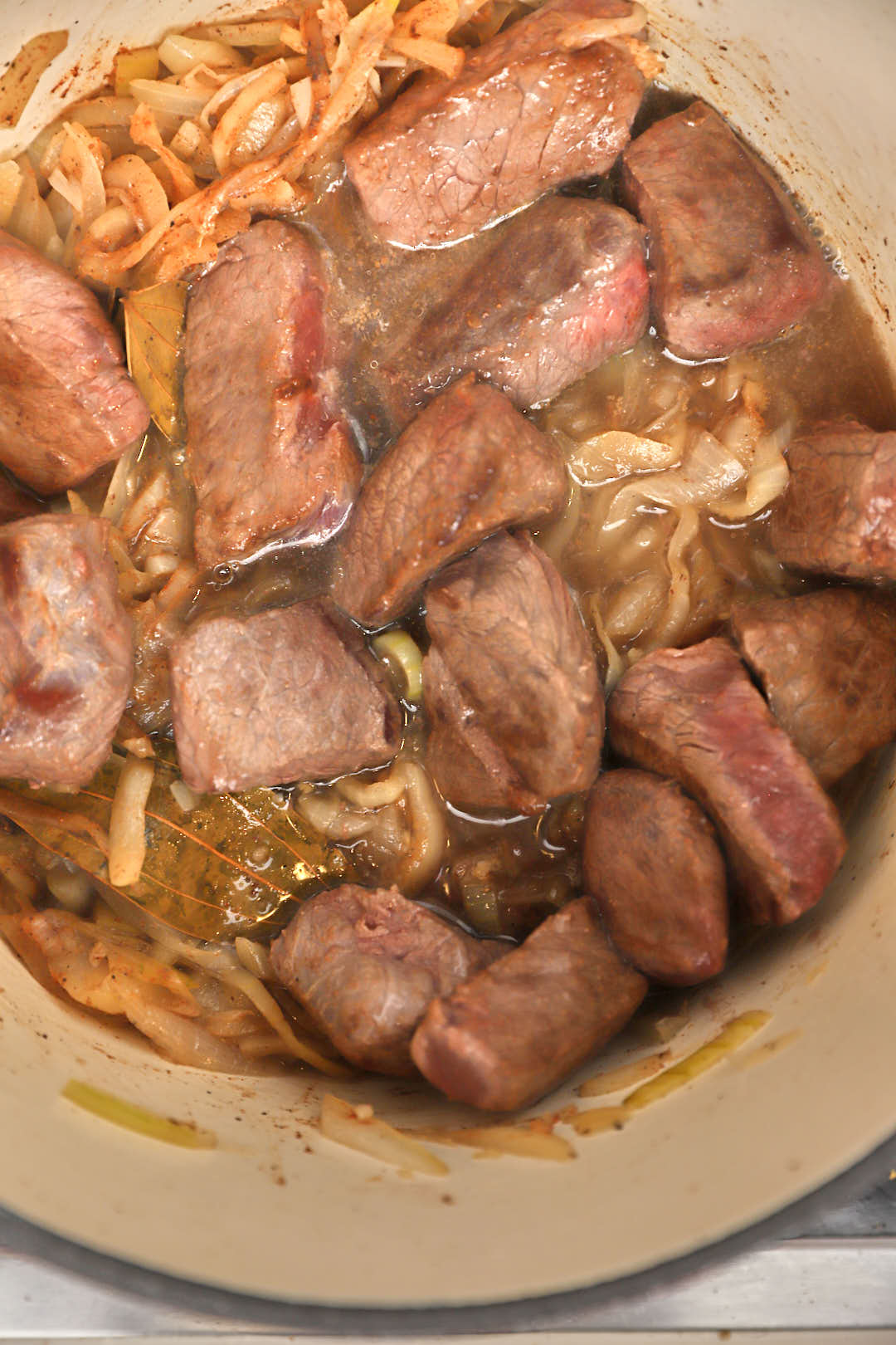 Water added to beef cubes and sauteed onions in a pot.