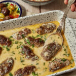 kofta with tahini sauce in a pan with a spoon scooping some out