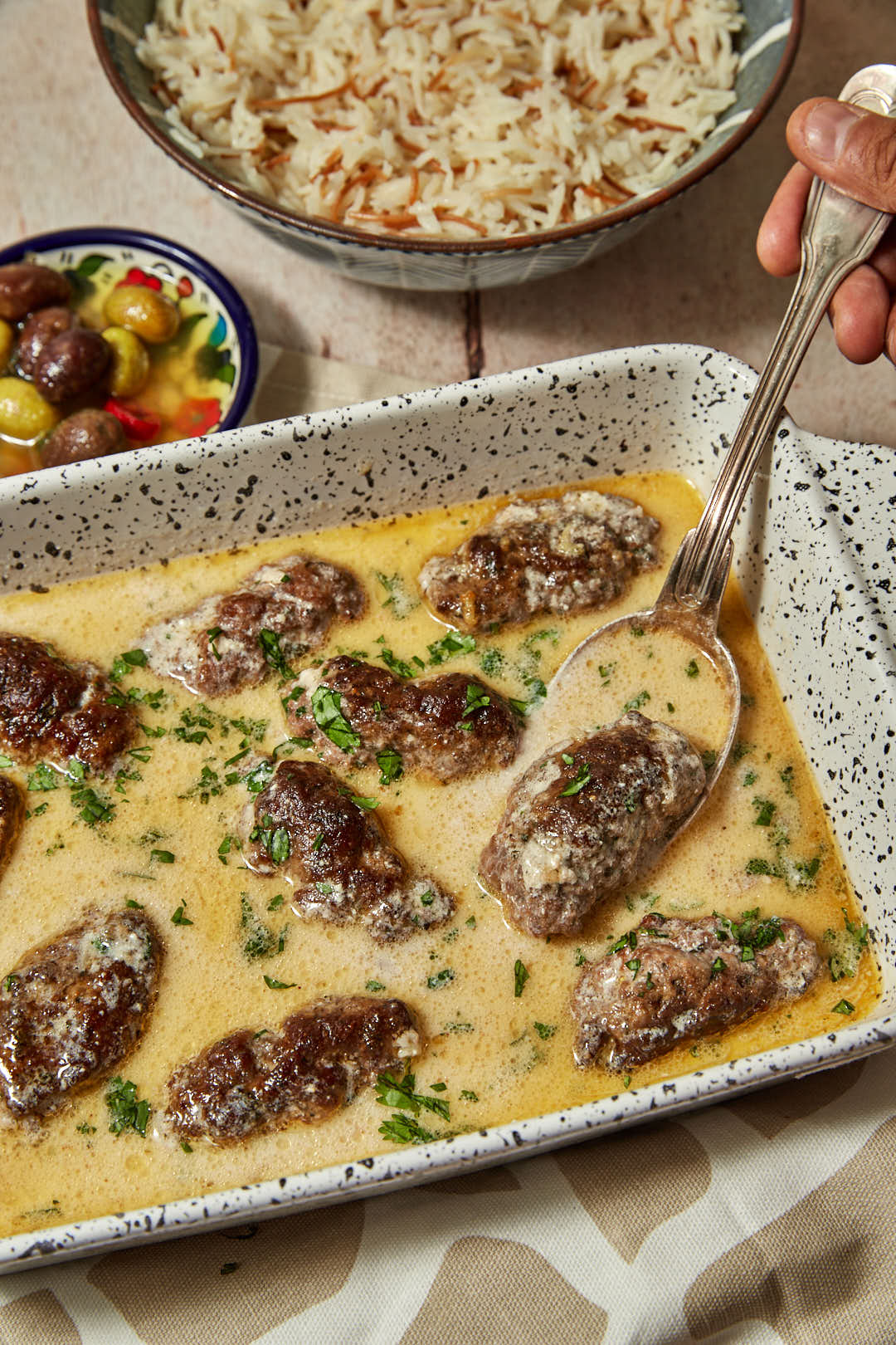 kofta with tahini sauce in a pan with a spoon scooping some out