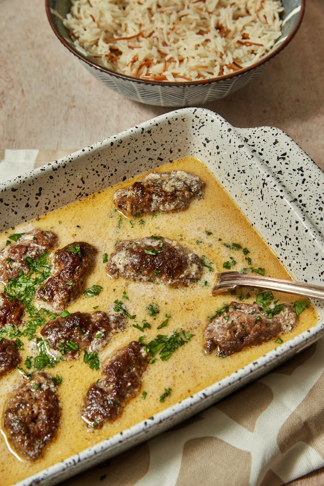 a big pan of kofta with tahini sauce with vermicelli rice in the background.