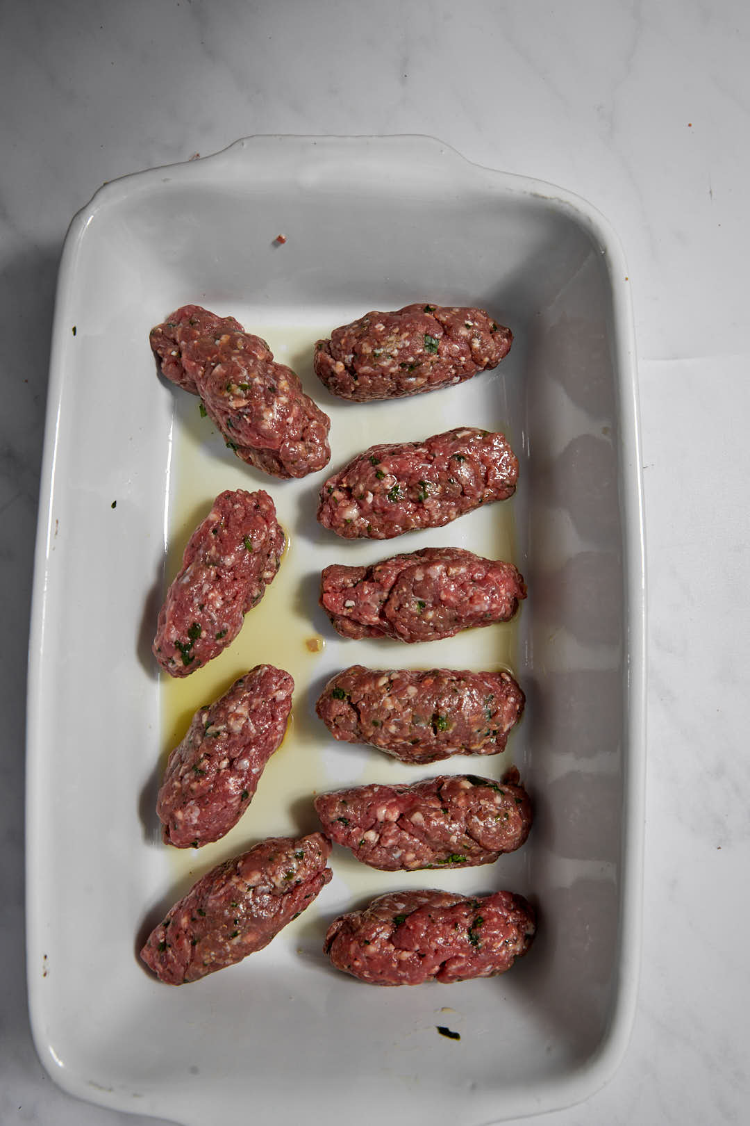 kofta formed into patties in a white baking dish.