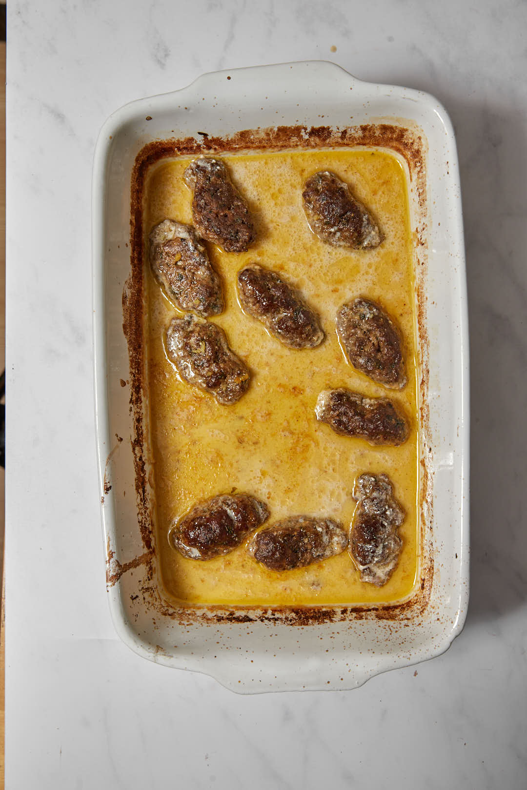 baked tahini sauce with kofta in a white pyrex dish.