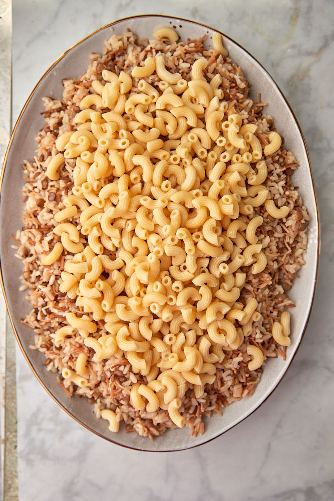 Elbow macaroni on top of lentils and rice in serving platter.