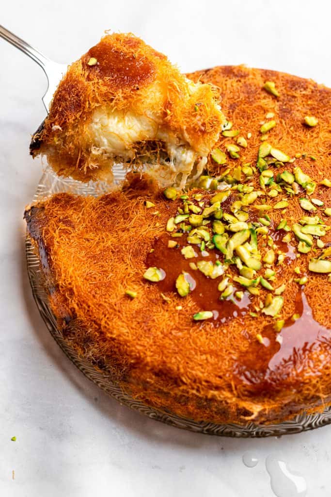 Kunafa drizzled with sugar syrup being lifted out of a plate