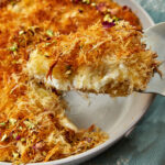 a slice of cream kunafa being lifted out of a cake pan.