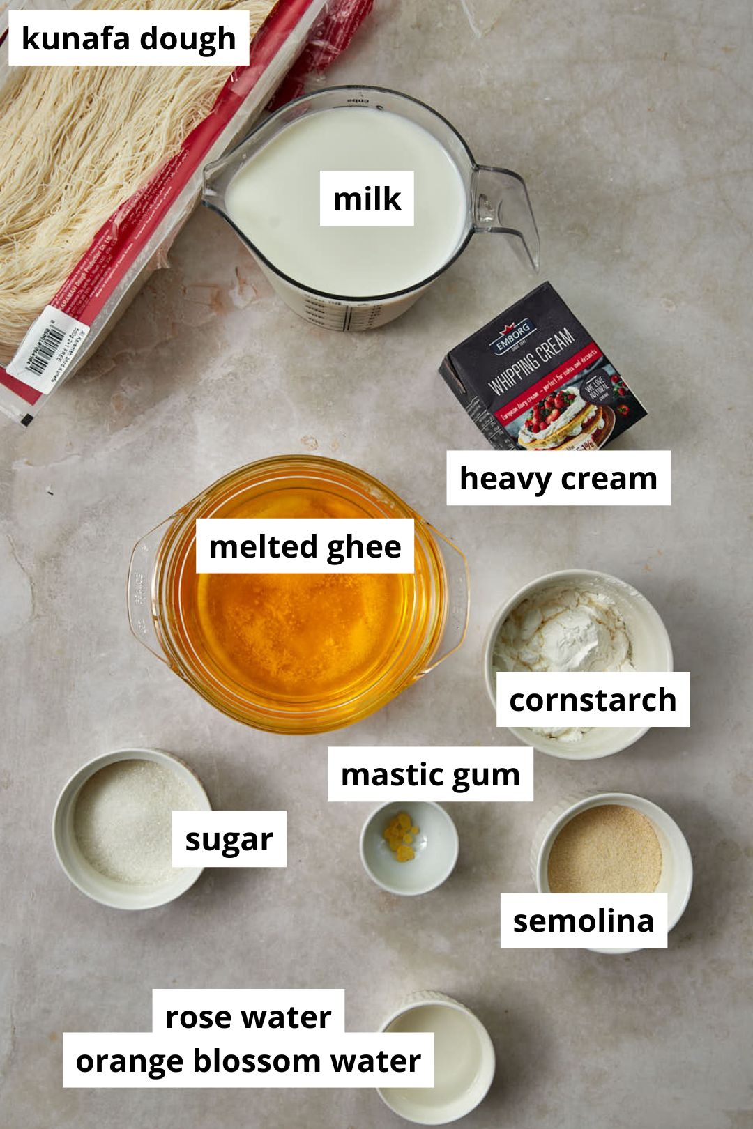 Ingredients needed to make kunafa with cream on a light marble background.