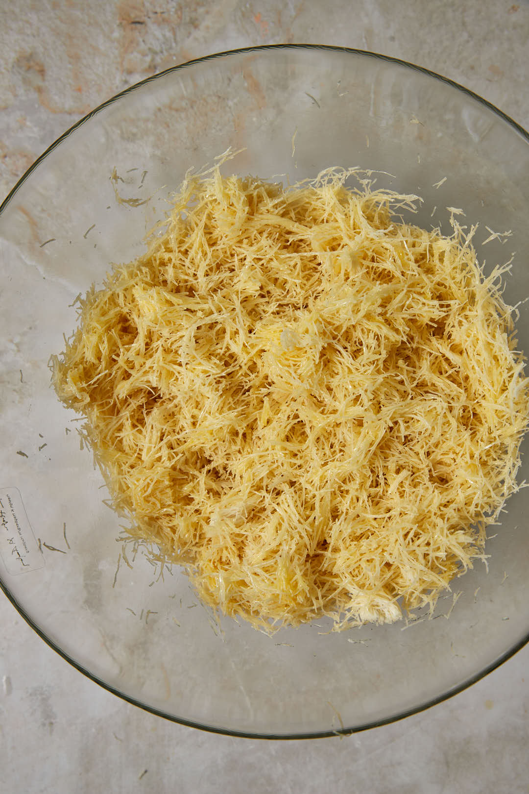 kunafa dough mixed with ghee in glass bowl.