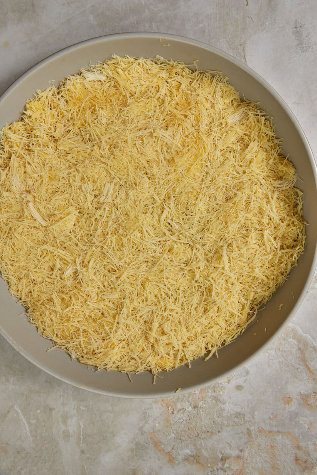 kunafa dough packed into a prepared pan, before baking.