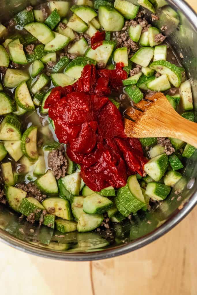 tomato paste and baby marrow in a saucepan with a wooden spoon