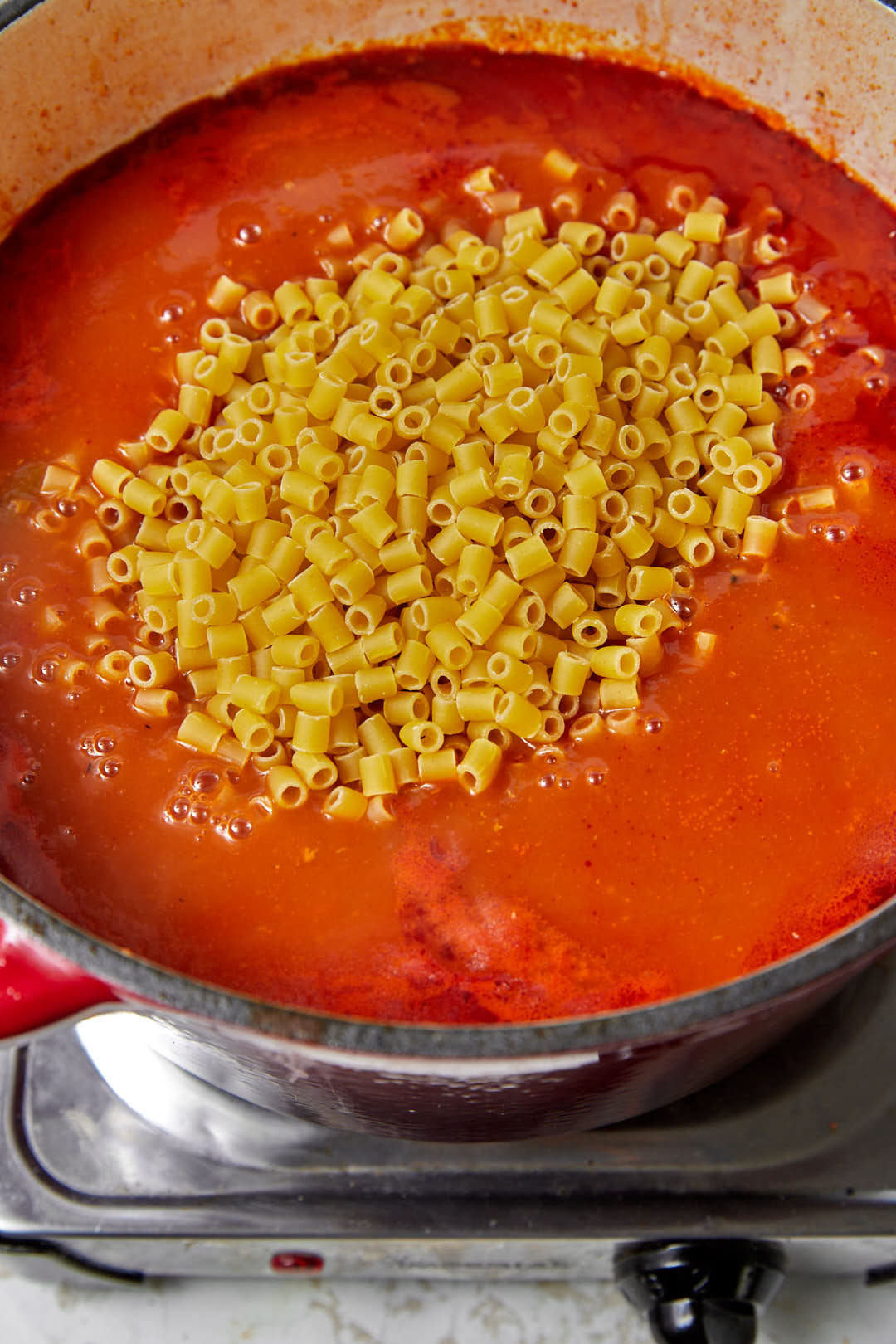 small tube pasta added to a simmering tomato sauce in a saucepan.