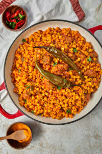 top shot of libyan mbakbaka pasta on a white kitchen towel with chili peppers and some turmeric in small bowls on the side.