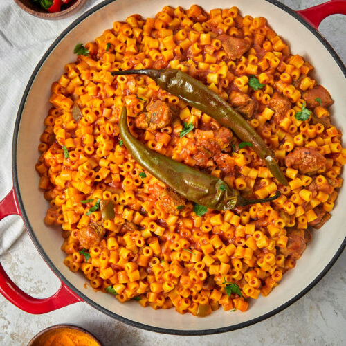 top shot of libyan mbakbaka pasta on a white kitchen towel with chili peppers and some turmeric in small bowls on the side.