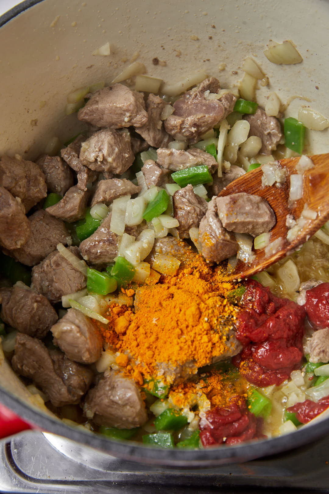 turmeric powder, spices and tomato paste added to bell peppers and onion and meat cubes in a saucepan.