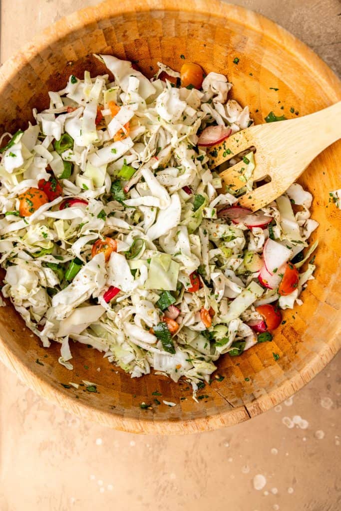 cabbage salad being tossed in a wooden bowl