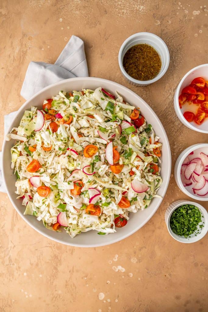 lebanese cabbage salad in grey bowl with topping ingredients in small bowls