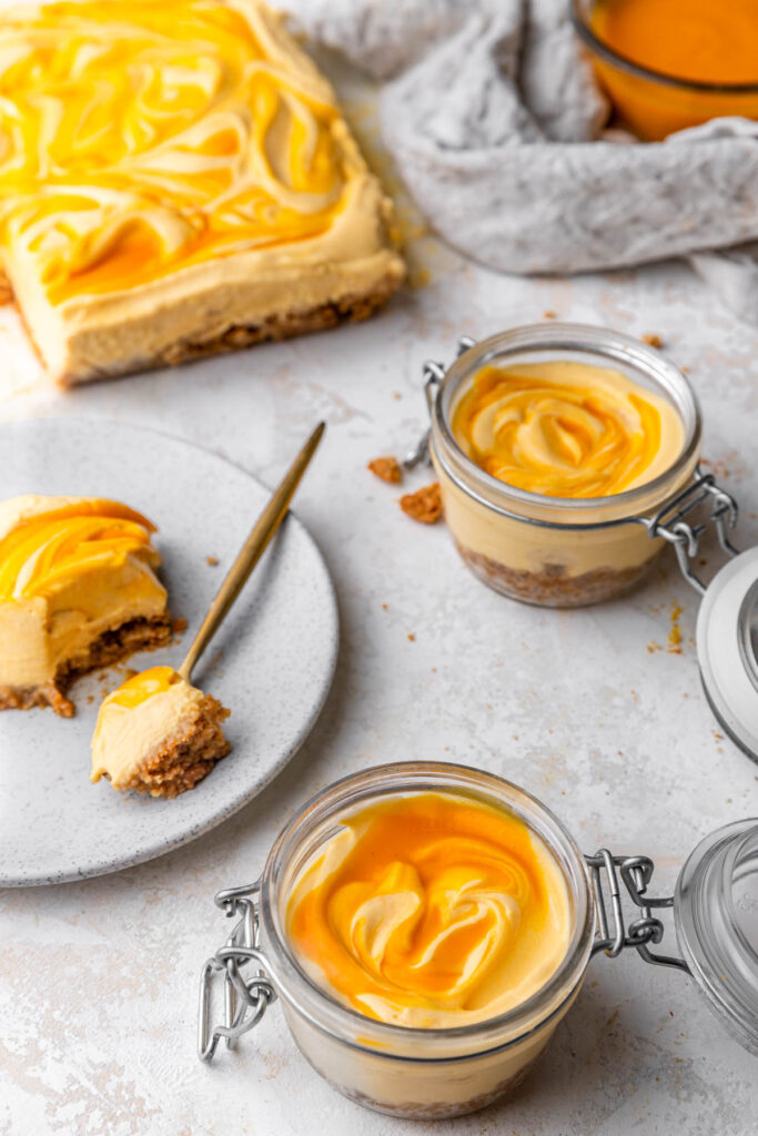 no bake mango cheesecake in jars and in bar form with a slice taken out.