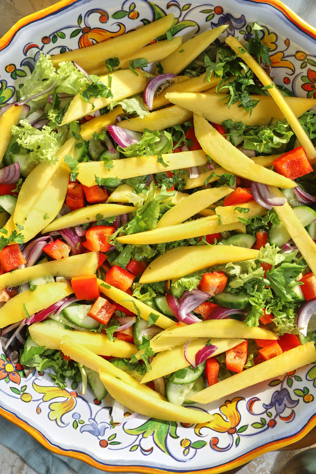 mango, bell pepper, onions, and cucumber on lettuce in a large platter.