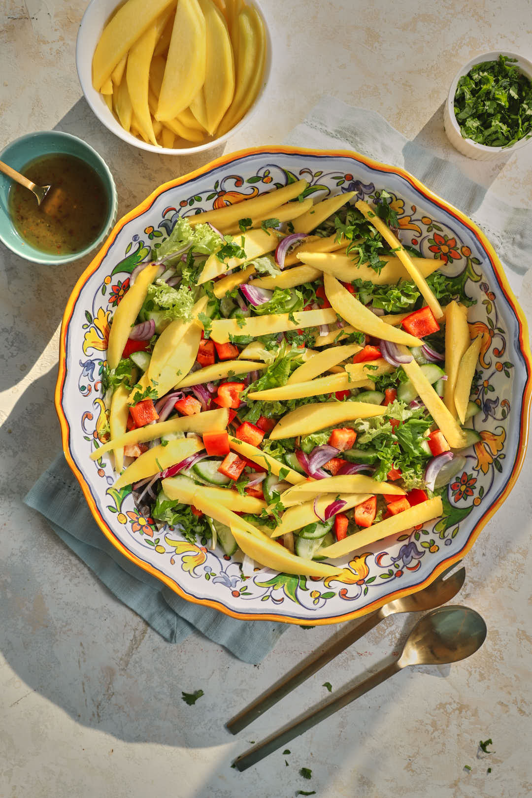 photo of a lettuce and mango salad in a large platter on a blue kitchen linen and on a white background.
