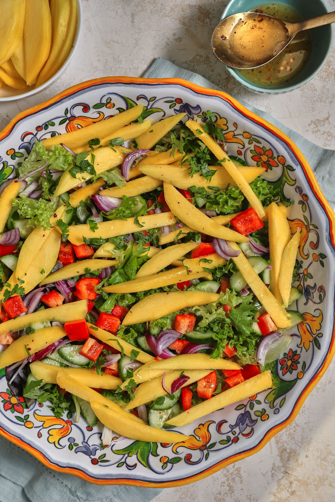 mango cucumber lettuce salad in a white platter with extra mango in the background.