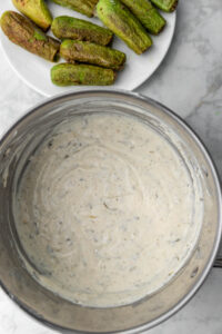 Pot of middle eastern yogurt sauce with zucchini on a plate in the background.