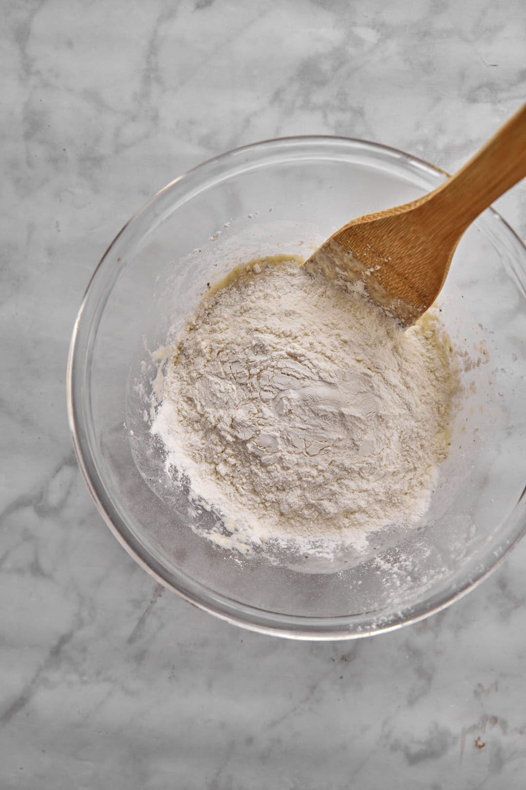 flour and dough in a clear bowl with a wooden spoon.