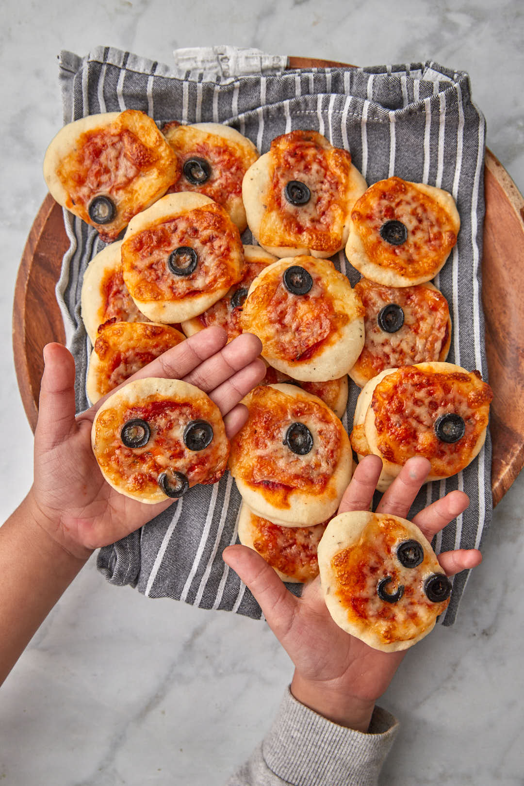 two kids hands holding a mini pizza in each hand.