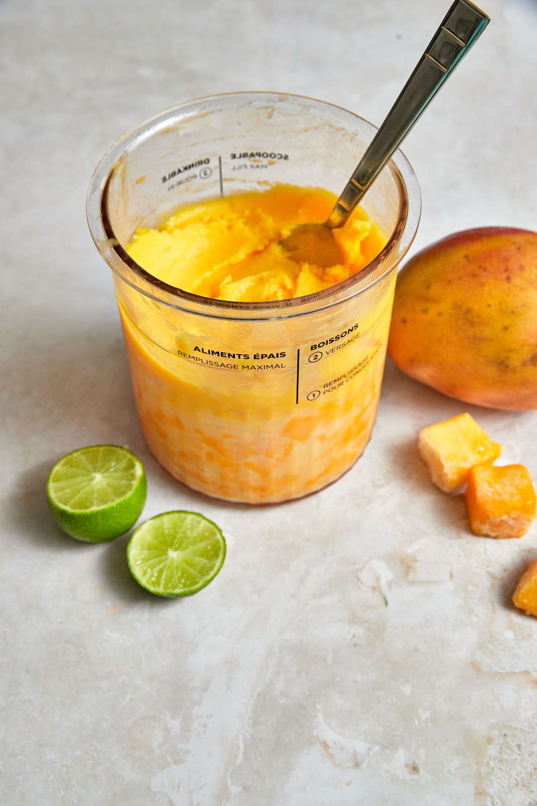 a ninja creami pint with mango sorbet in it, mangoes and limes in the background.