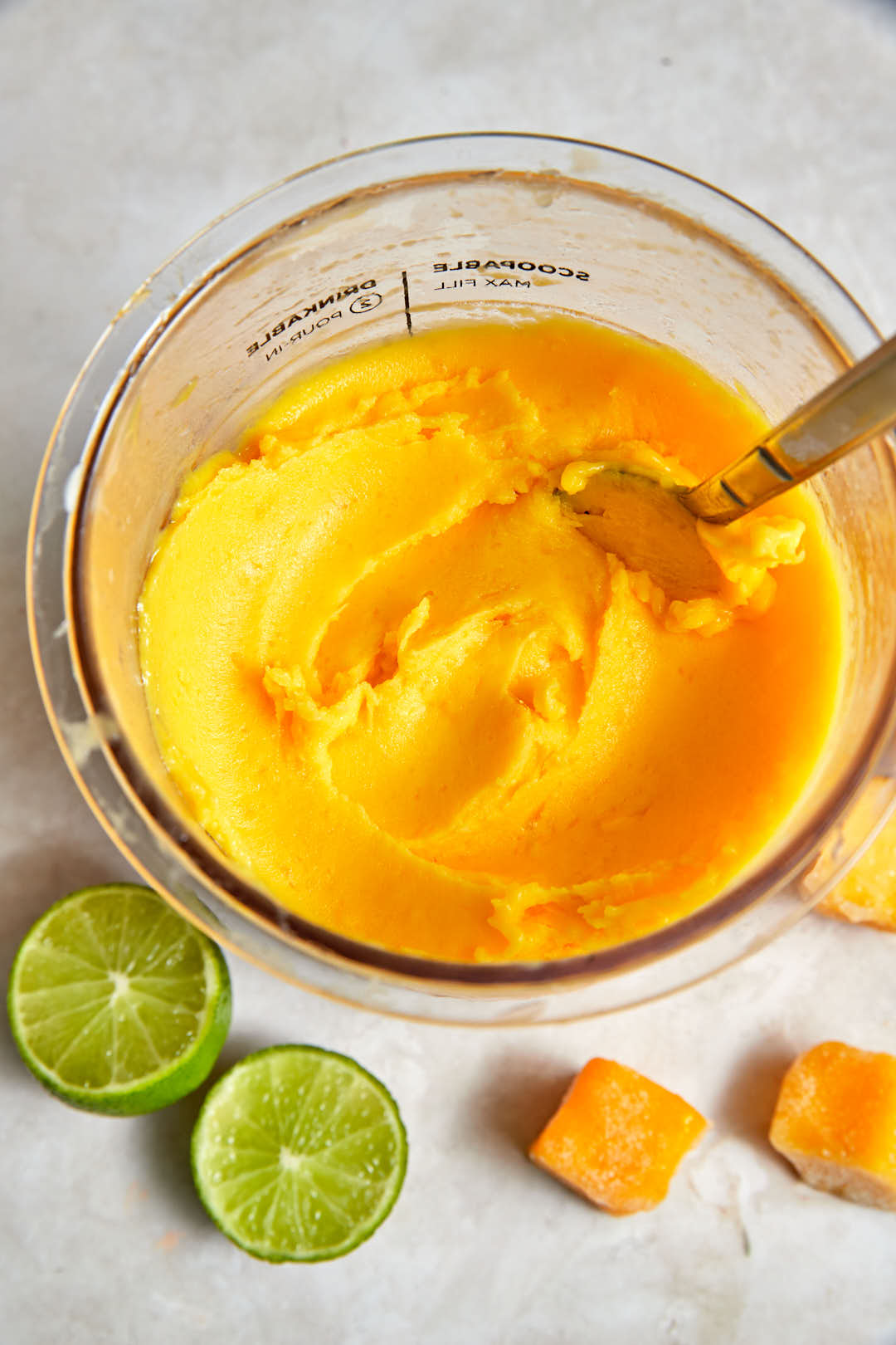 top shot of ninja creami mango sorbet with mango cubes and limes in the background.