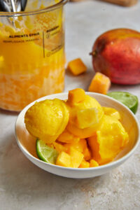 mango sorbet piled high in a bowl with mango cubes and a lime wedge.