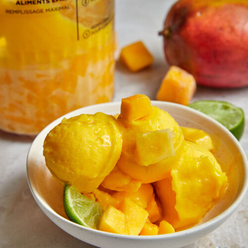 mango sorbet piled high in a bowl with mango cubes and a lime wedge.