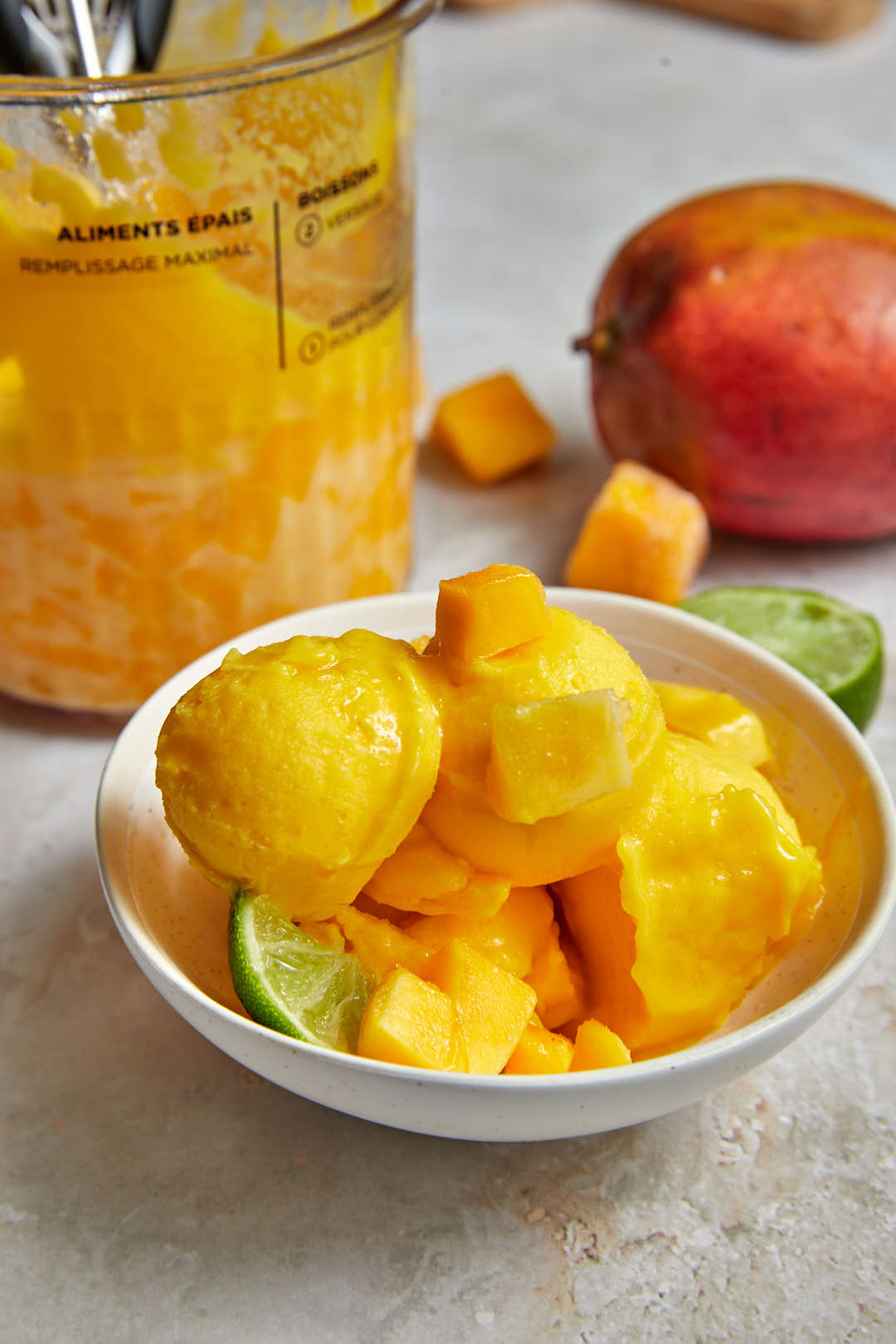 mango sorbet piled high in a bowl with mango cubes and a lime wedge.