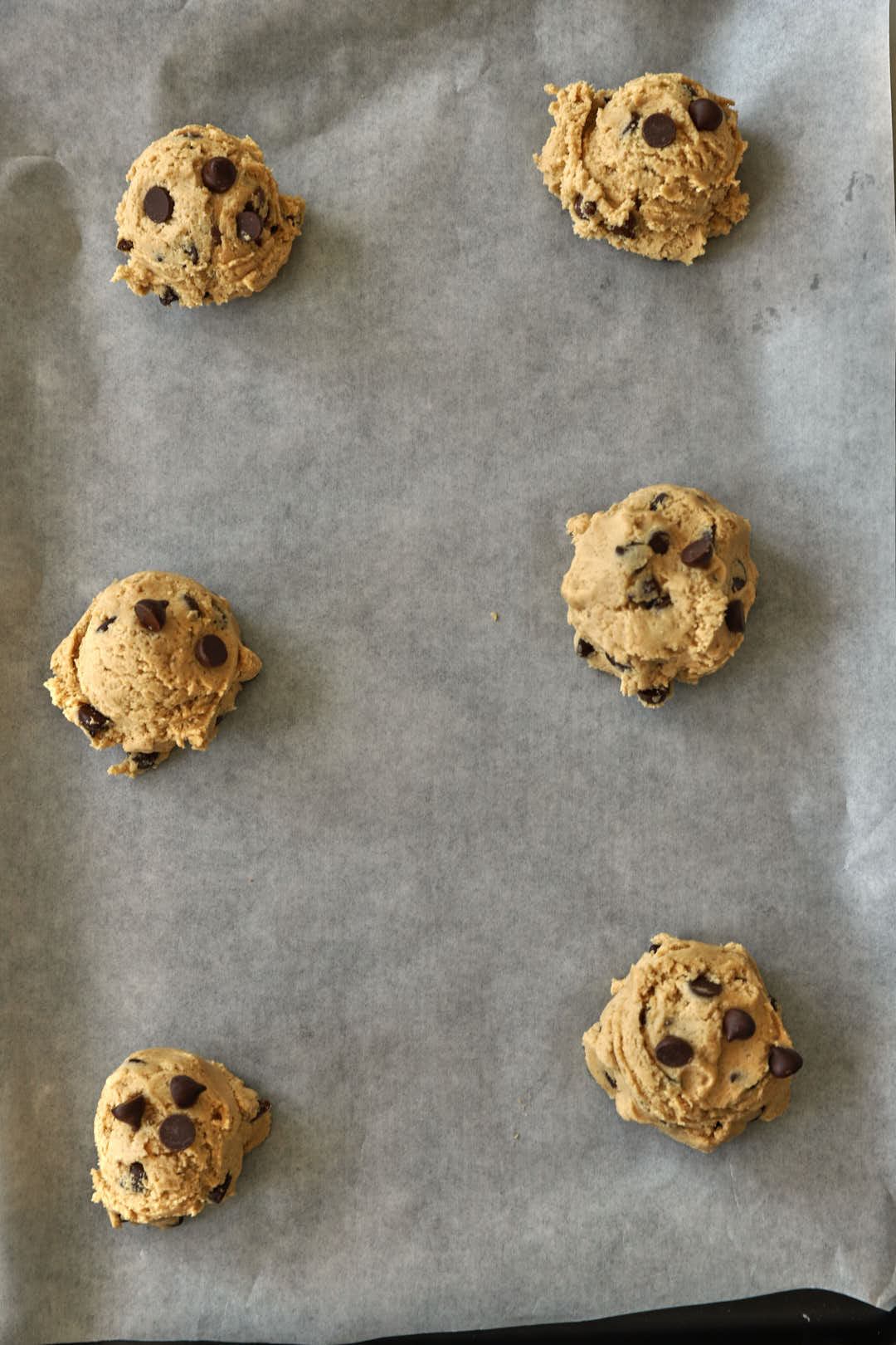 chocolate chip cookie dough balls on parchment paper on a baking sheet.