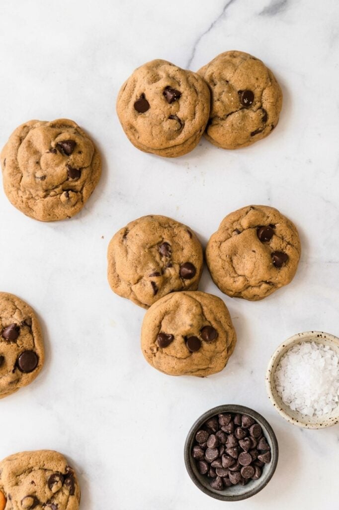chocolate chip cookies on a white background with a small bowl of flaky sea salt and one of chocolate chips.