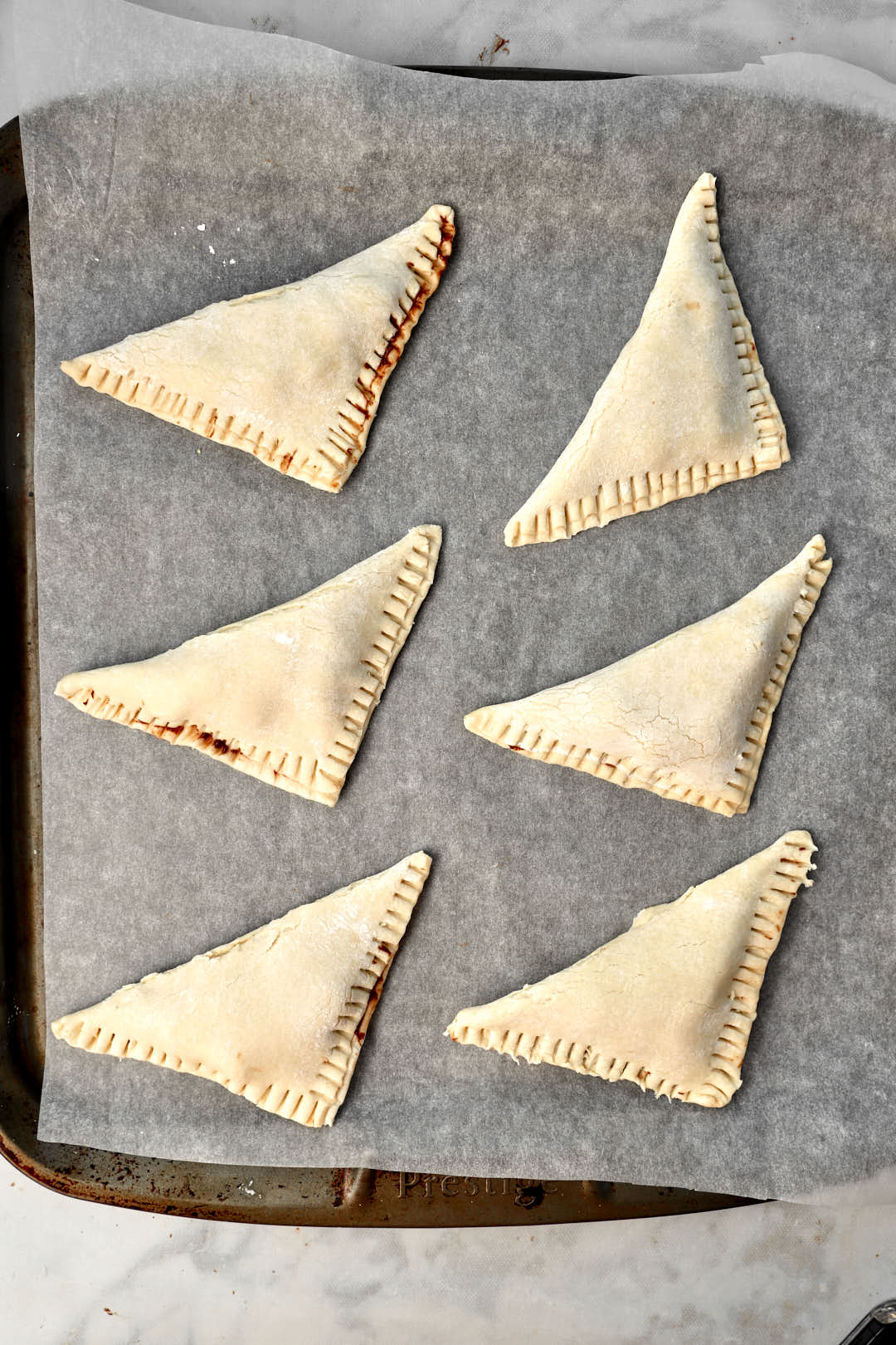 Nutella turnovers on parchment paper lined baking sheet with crimped edges before baking.
