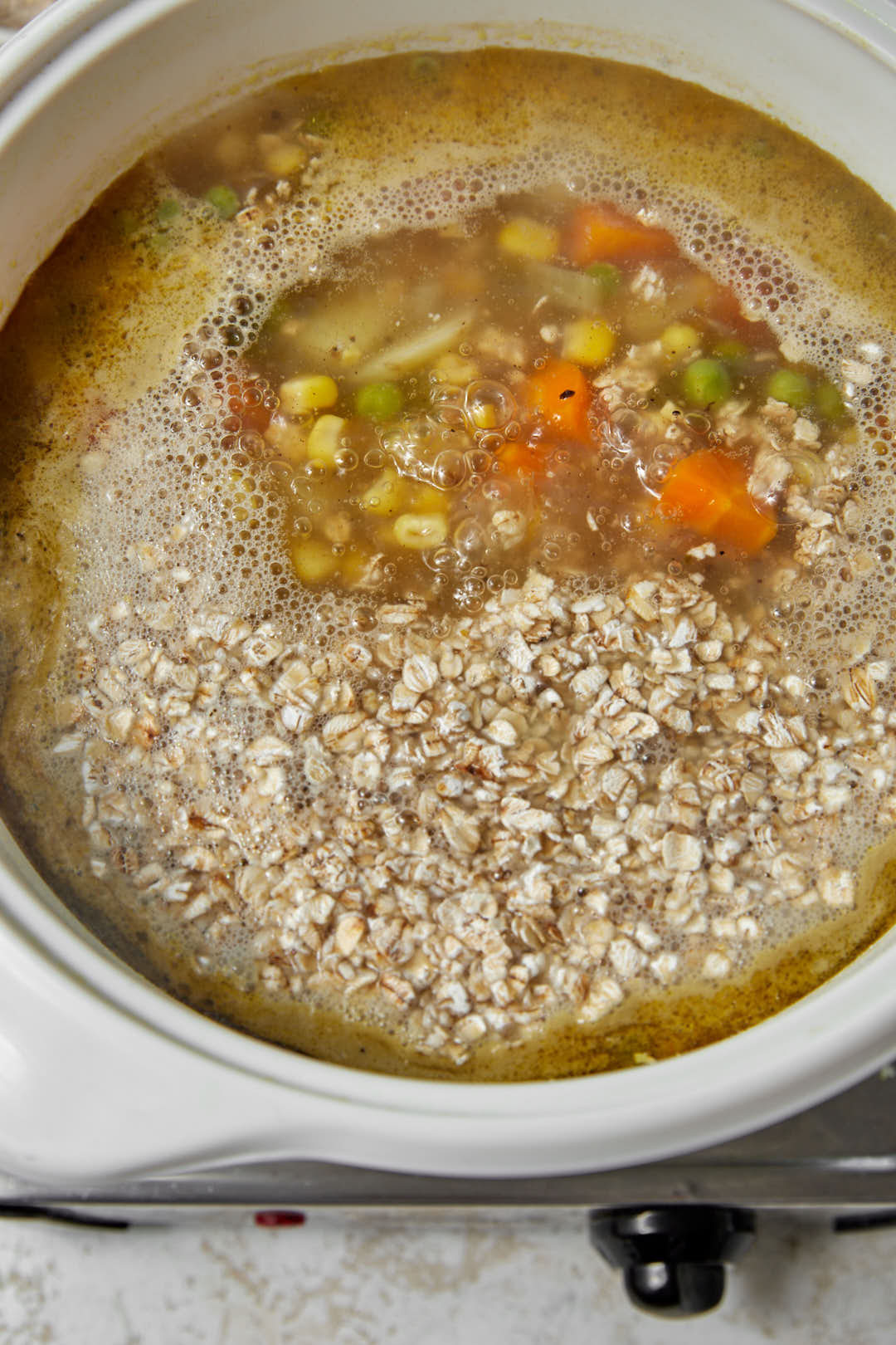 oats added to vegetables and broth in a saucepan.