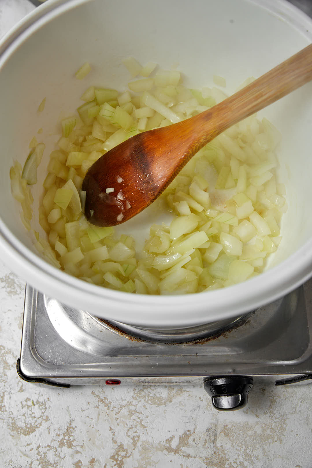 sauteed onions in a white pot with a wooden spoon.