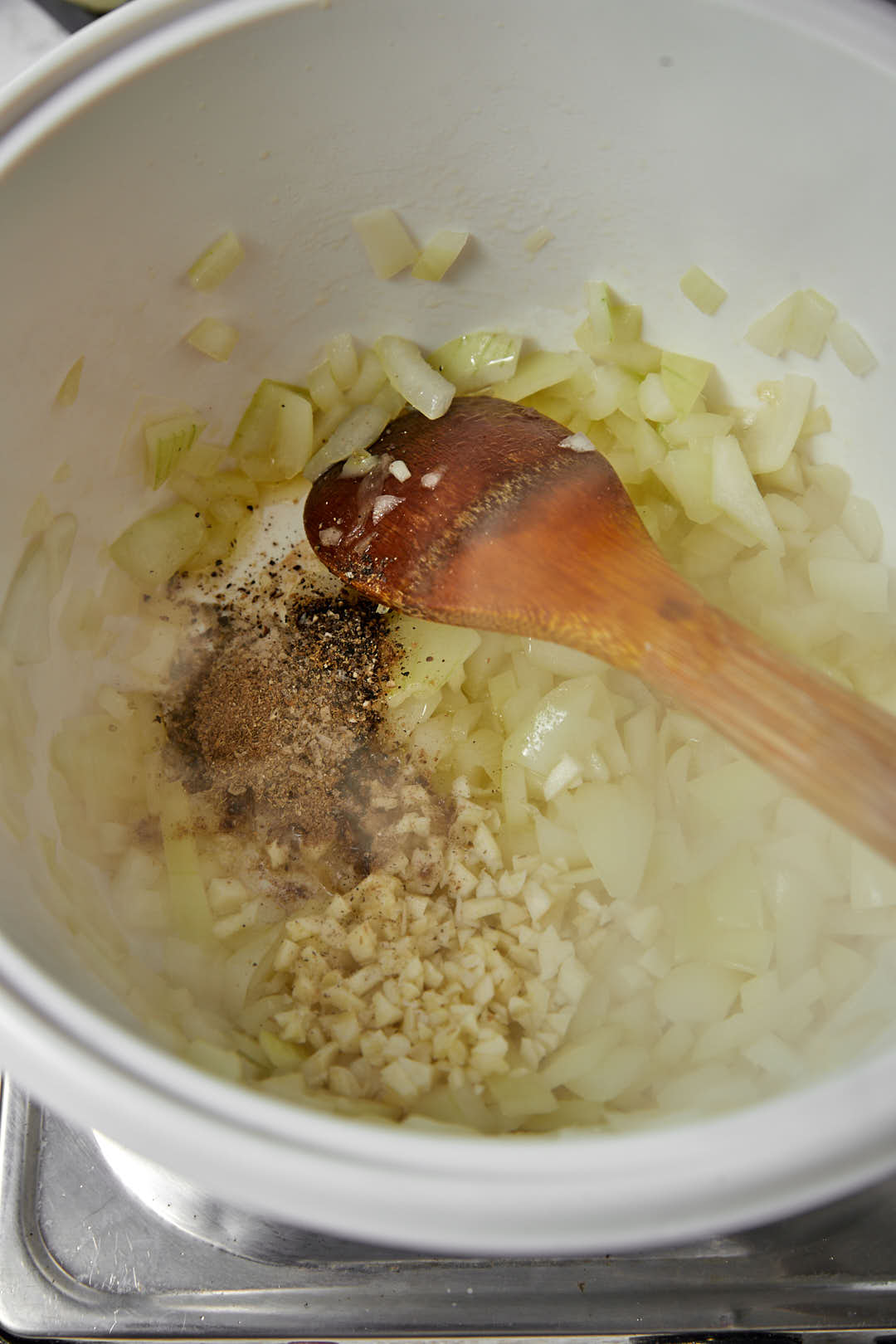 garlic and spice added to sauteed onions in a white pot.