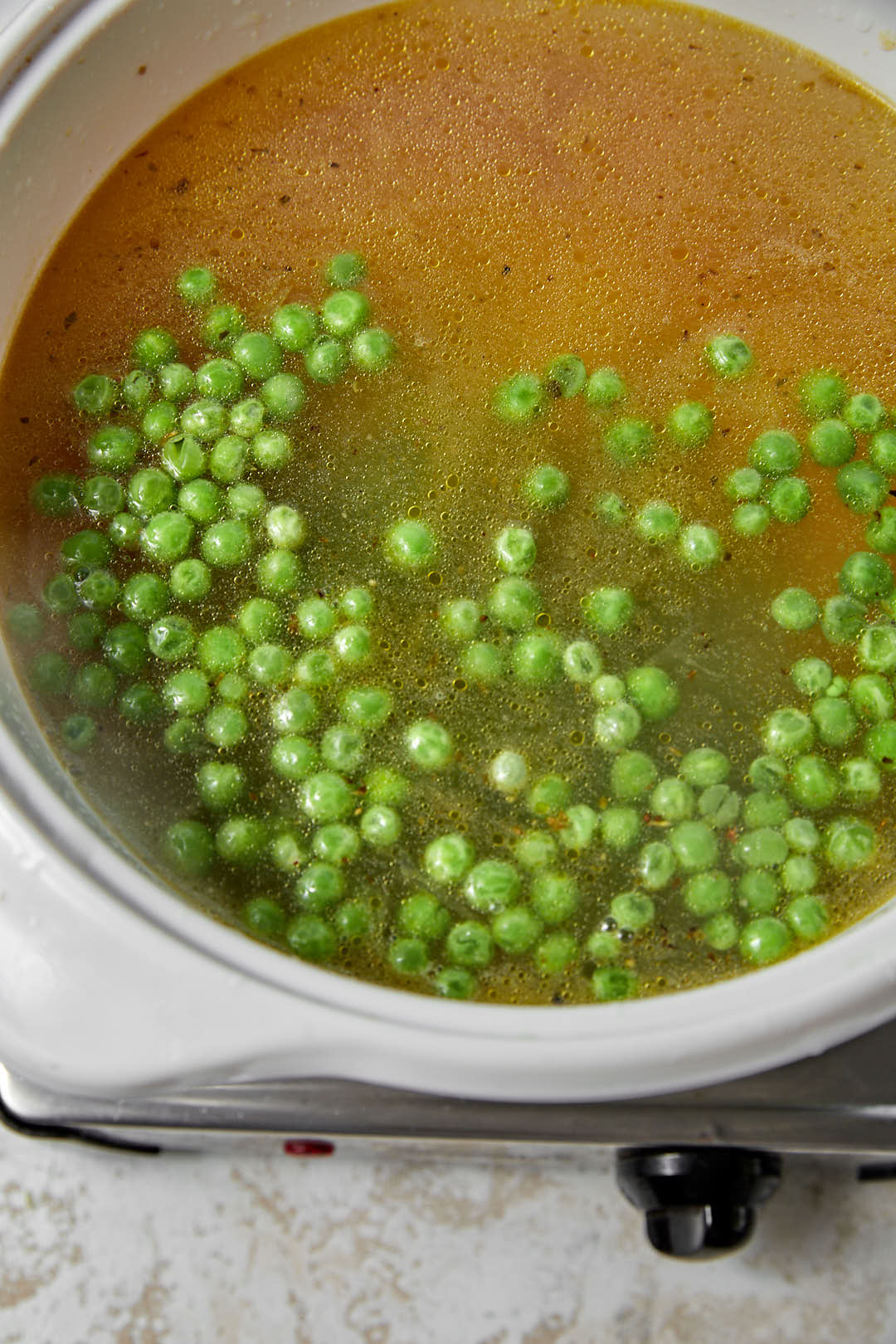 frozen peas on vegetable broth in a white pot.