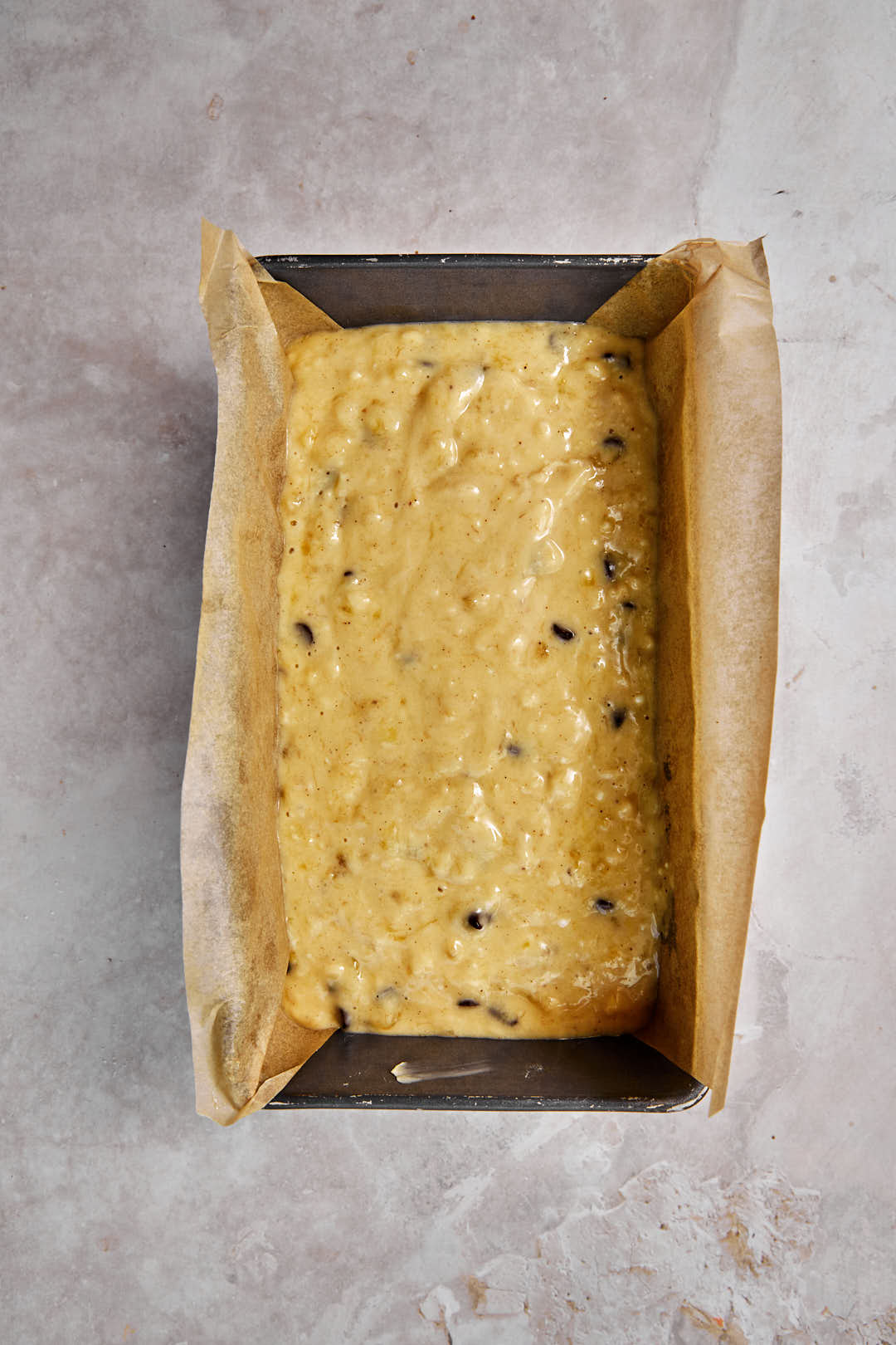 banana bread batter in a loaf pan with parchment paper.