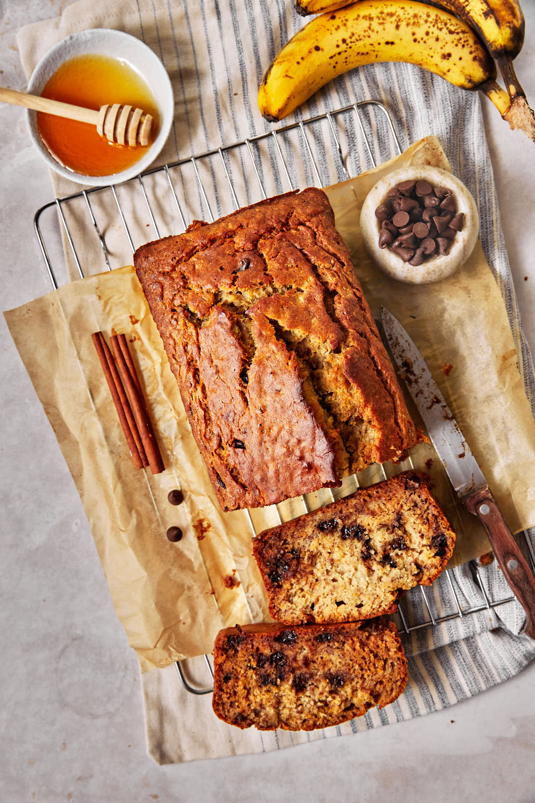 top down photo of a loaf of banana bread sliced, on parchment paper with a small bowl of chocolate chips on the side.