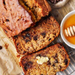 close up photo of sliced olive oil banana bread with a pat of butter on one slice and a little honey in a dish on the side.