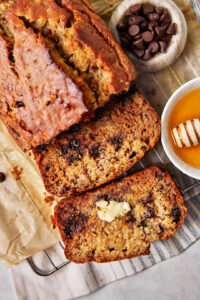 close up photo of sliced olive oil banana bread with a pat of butter on one slice and a little honey in a dish on the side.