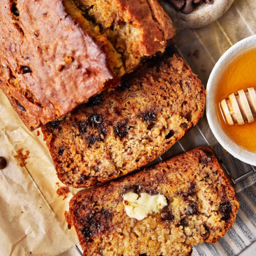 close up photo of sliced olive oil banana bread with a pat of butter on one slice and a little honey in a dish on the side.