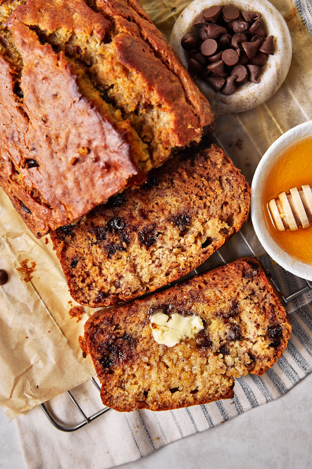 close up photo of sliced olive oil banana bread with a pat of butter on one slice and a little honey in a dish on the side.