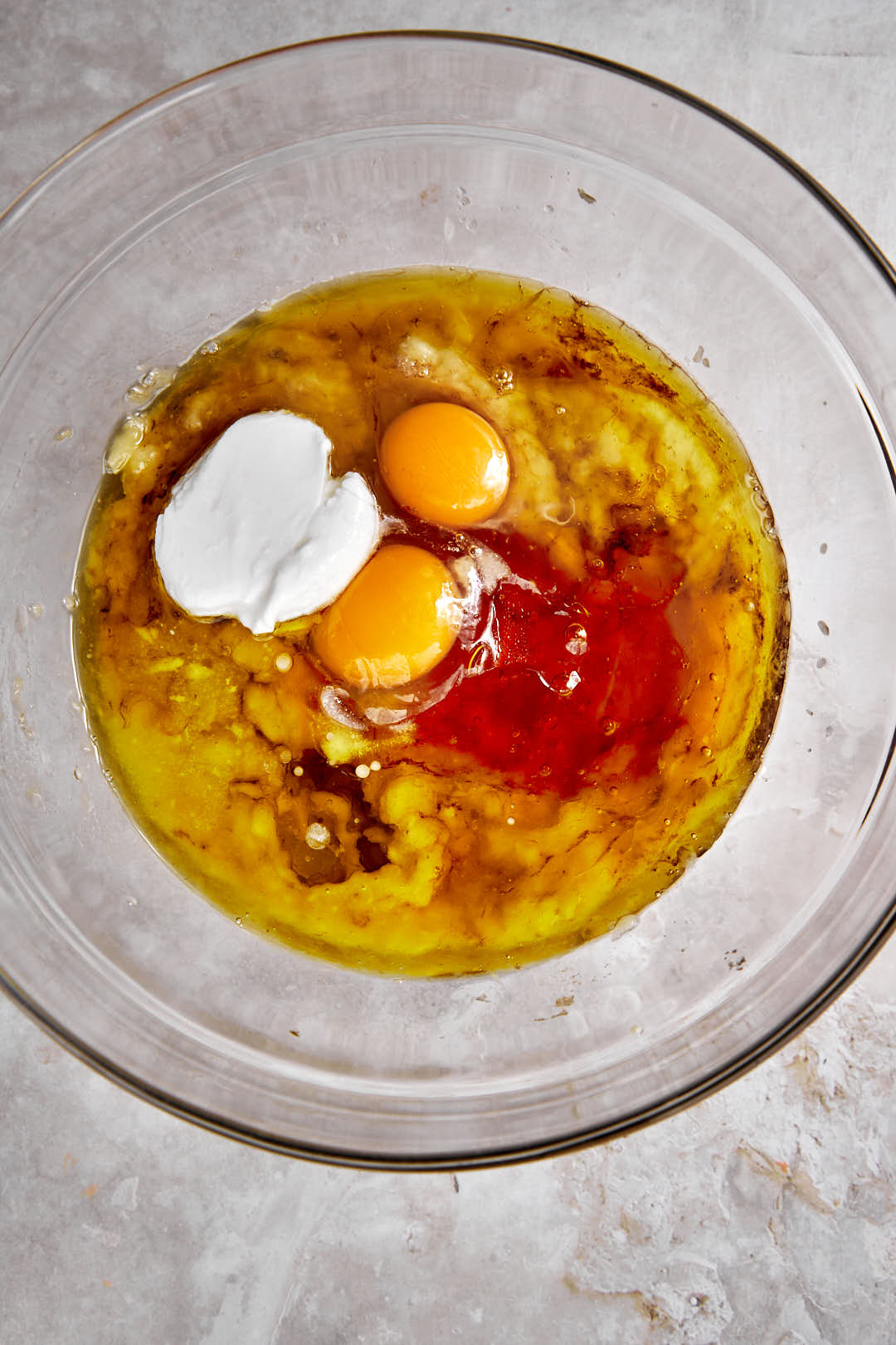 eggs, yogurt, honey and olive oil added to mashed banana in a glass bowl.