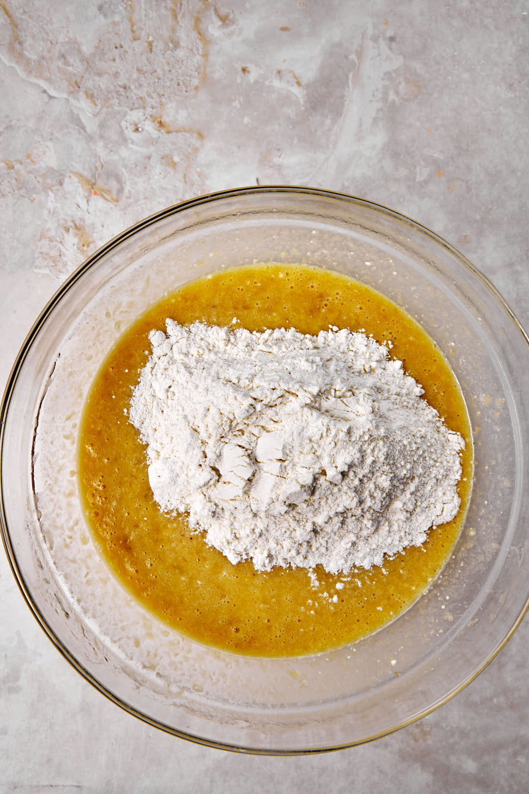 flour added to banana bread batter in a glass bowl.