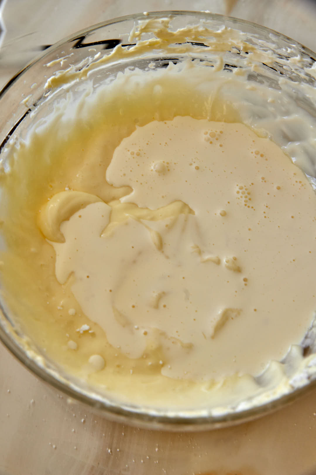 heavy cream added to a cream cheese mixture in a glass bowl.