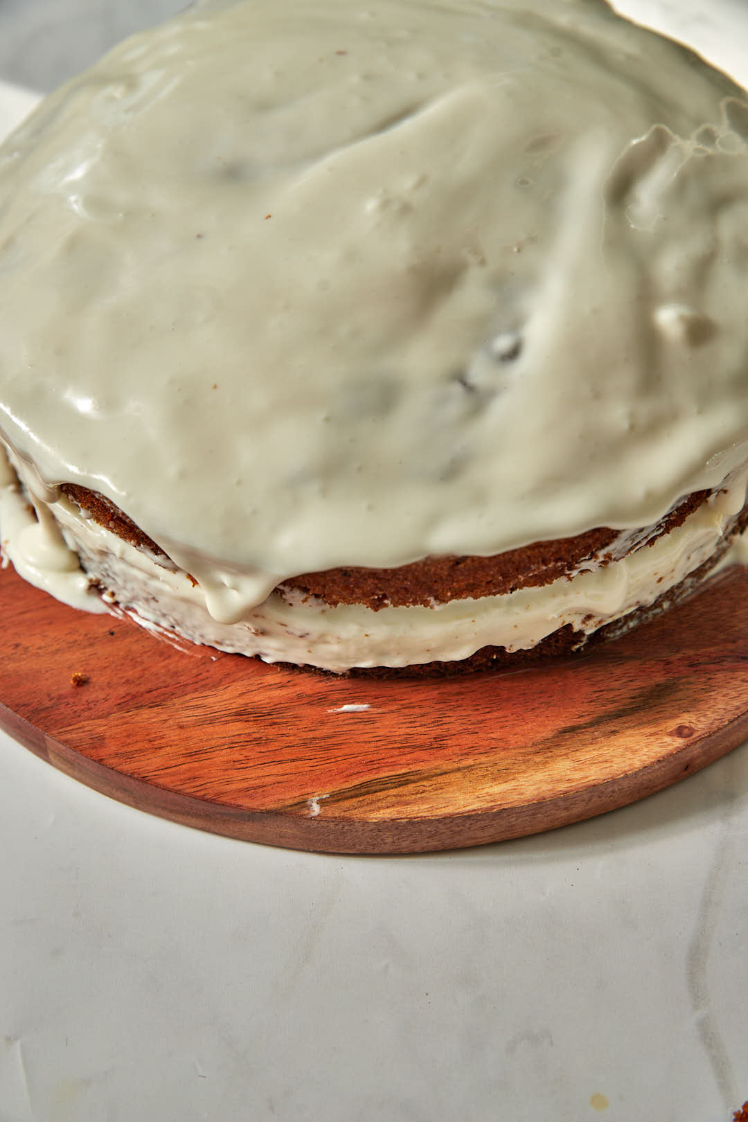frosted carrot cake on a wooden plate before garnishing.